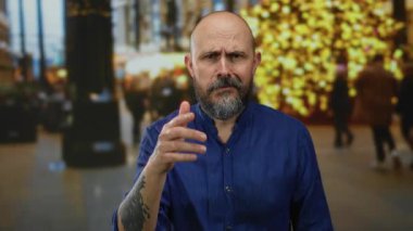 Mavi tişörtlü, sakallı bir adam. Bulanık ışıklarla şehir sokağında endişe ediyor..