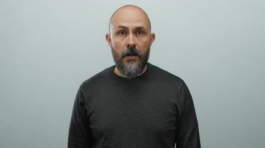 Kel sakallı, beyaz yüzlü beyaz bir adam kameraya bakarken beyaz arka planda siyah bir kazak giyiyor..