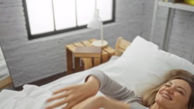 Kadın, rahat yatak odasındaki beyaz yatakta keyifle dinleniyor. Huzurlu bir sabah geçiriyor. Huzur veren doğal ışık, huzur veren uzayın etrafını sarıyor..