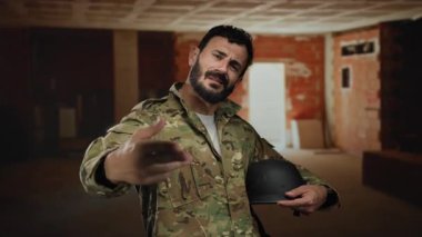 İspanyol üniformalı bir adam bir inşaat sahasında elinde miğfer tutarak kısmen inşa edilmiş iç kısımda odaklanmış bir ifade sergiliyor..