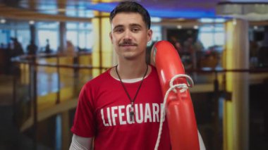 Modern kapalı otel ortamında kendine güveni olan genç İspanyol cankurtaranın elinde şamandıra var.