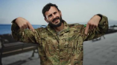 İspanyol üniformalı bir adam kumsalda geziniyor, ciddi bir ifadeyle aşağıya bakıyor, arkasında bir kıyı şeridi olduğunu düşündüren okyanus var..