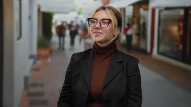 Kadın dürbünle hareketli şehir caddesinde gözlük ve siyah palto takarak hareketli hareketli hareketler yapıyor. Etrafı parlak şehir atmosferini yansıtan yayalar ve dükkanlarla çevrili..