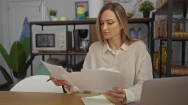 Konforlu ofis ortamında arka planda bitki ve raflarla dokümanları inceleyen kadın, odaklanmış bir çalışma ortamı sergiliyor.