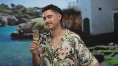 İspanyol adam deniz kenarında dondurma yiyor, tropikal bir geçmişi var, renkli bir gömlek giyiyor, güneşli bir günde deniz kenarında neşeli bir tatil havası yaratıyor..