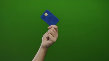 Beyaz adamın yeşil arka plana karşı mavi kredi kartı var, finansal temalar ve basitlik vurgulanıyor.