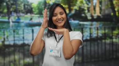 Beyaz gömlekli, parkın arka planında gülümseyen Latin bir kadın açık hava manzarası, rahat yaz havası ve arkadaş canlısı tavırlar sergiliyor..