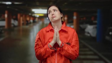 Elleri kelepçeli turuncu hapishane tulumlu kadın arka planda arabalarla loş bir otoparkta yalvarırken dramatik bir hukuki sahneyi yakalıyor..