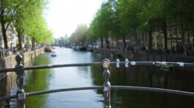 Bulanık ağaçlar ve su yolu boyunca uzanan binalarla Amsterdam Kanalı 'nın bulanık görüntüsü Hollanda' daki ikonik köprü ve canlı şehir atmosferini gözler önüne seriyor..