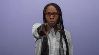 Gözlüklü, örgülü, mor duvara kızgın bir şekilde bakan kadın güçlü bir duygu ifadesi sergiliyor. Kendine güvenen bir tavır sergiliyor..