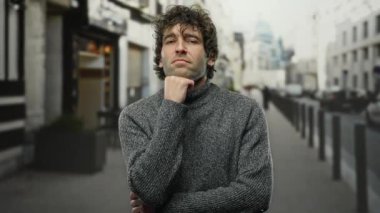 Gri kazaklı yakışıklı adam kapalı gözleri ve düşünceli ifadesiyle şehir yalnızlığının somutlaşması ve iç gözlem ile şehir caddesinde düşünceli bir şekilde duruyor..