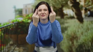 Yeşil bir parkta dikilirken orta parmaklarıyla jest yapan bir kadın, aydınlık bir günde açık havada yakalanan bir ortamda hayal kırıklığı ve tavır sergiliyor..