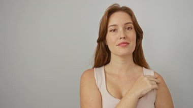 Beyaz arka planda düşünceli bir şekilde gülümseyen kadın, sakin bir ifadeyle güzellik ve özgüven sergiliyor ve izole bir ortamda kızıl saçlı..