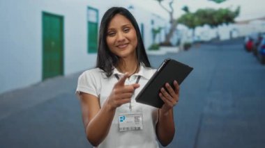 Sokakta elinde tabletle kameraya gülümseyen bir kadın neşeli bir ifade sergiliyor..