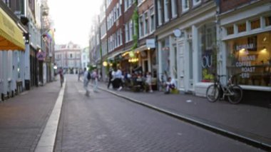 Amsterdam 'da, tarihi binalar, kafeler ve rahat bir atmosferle çevrili kaldırım taşlı bir sokakta gezinen insanların olduğu bulanık şehir manzarası..