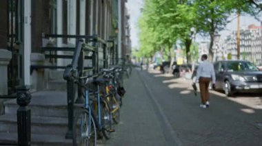 Açık hava Avrupa şehir caddesinin bulanık manzarası. Odaklanmış bisikletler ve arka planda ağaçlarla kaplı kaldırım boyunca yürüyen bir adam. Bokeh etkisi yaratıyor..