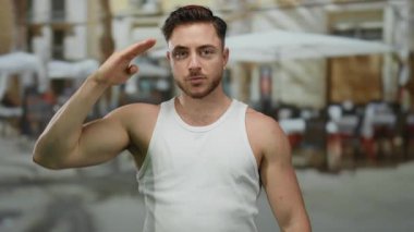 Şehir restoranının terasında oturan sakallı genç adam arka planda bir sokak dekorunu gösteriyor..