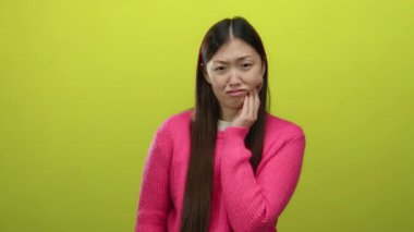 Dişi ağrıyan, sarı arka planda pembe süveter giyen Asyalı kadın acı ve rahatsızlığını dile getiriyor..