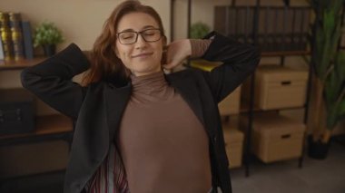 Ofis koltuğunda rahat bir şekilde gülümseyen genç iş kadını, iyi organize edilmiş bir ofis ortamında pozitif bir çalışma ortamı öneriyor..