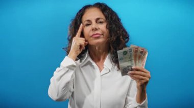 Orta yaşlı bir kadın mavi arka planda İngiliz banknotları tutuyor..