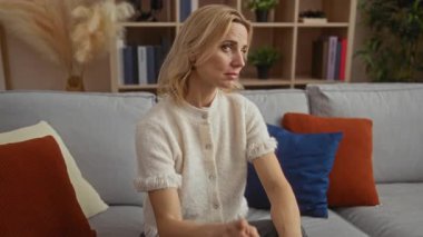 Hayır diyen bir kadın, modern apartmandaki renkli yastıklarla çevrili bir kanepede otururken rahat oturma odasında parmağını göstererek işaret ediyor.