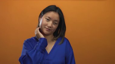 Genç Çinli kadın, izole edilmiş turuncu bir arka plana karşı düşünceli bir şekilde poz veriyor. Mavi elbiseli..