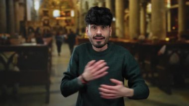 Tarihi kilise ortamında şaşkın bakışları olan genç bir adam, süveter giyiyor, kapalı bir arkaplanda duygularını sergiliyor..