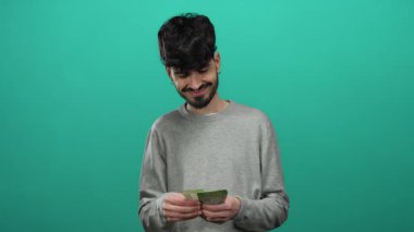 Elinde Rus rublesi banknotlar tutan bir adam izole edilmiş yeşil duvarlara gülümsüyor. Gri kazaklı..