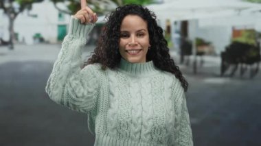Genç İspanyol kadın, gündüz vakti şehir sokaklarında dikilirken heyecanla gülümsüyor ve işaret ediyor.