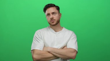 Sakallı ve beyaz gömlekli genç adam izole edilmiş yeşil arka plan duvarına karşı düşünceli bir şekilde duruyor. Kollarını kavuşturmuş dalgın dalgın dalgın duruyor..