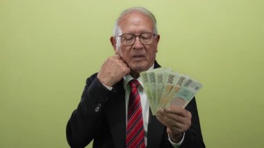 Takım elbiseli kıdemli bir adam, Koruna 'nın paralarını izole edilmiş sarı bir arka plan üzerinde incelikle tutuyor..