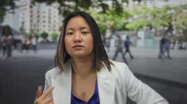 Yoğun bir şehir caddesinde hareketli genç Çinli kadın. Arka planda bulanık insanlar ve binalar var. Açık havada tutkulu bir konuşma yapıyor..