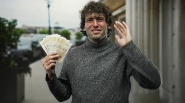 Şehirde Norveçli kronu tutan İspanyol bir adam dışarıda kulağını kapatırken acı veren bir ifade sergiliyor..