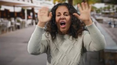 Canlı bir restoran terasında tutkulu kıvırcık saçlarıyla jestler yapan bir kadın, etkileyici hareketlerinde dikkat ve enerji yakalıyor..