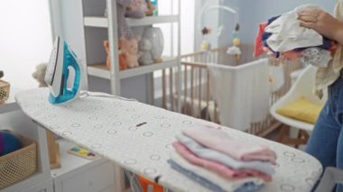 Temiz bir çamaşırhanede çamaşırlarını ütüleyen bir kadın, düzgün katlanmış çamaşırları ve parlak aydınlatılmış bir iç mekândaki ütüyle..