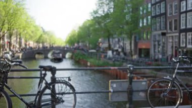 Bisikletler Amsterdam, Hollanda 'daki kanala bakan bir köprüde dinleniyor, büyüleyici evleri ve huzurlu bir su yolu hayal ürünü, bulanık bir şehir manzarası yaratıyor..