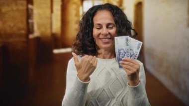 Açık hava üniversitesinde elinde Tayvan doları banknotları tutan izleyiciye doğru el kol hareketi yapan bir kadın klasik giyinmiş orta yaşlarda gülümseyerek finansal başarı öneriyor.