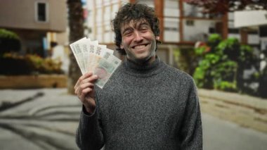 Şehirde İspanyol bir adam elinde neşeli bir ifadeyle Czech Koruna banknotları tutuyor. Arka planda binaları olan bir sokakta dikiliyor..