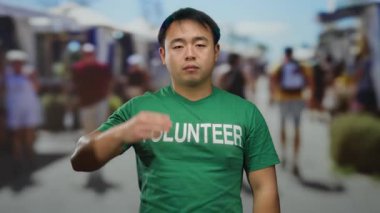 Yeşil tişörtlü genç bir adam açık hava pazarında gönüllü olarak mesaj atıyor..