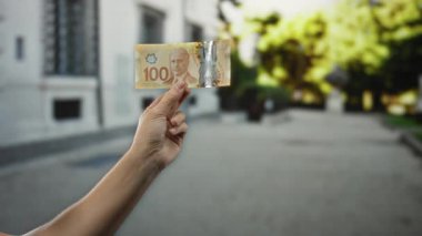 Bir şehir caddesinde Kanada banknotunu tutan, bulanık şehir geçmişine karşı canlı para gösteren, açık havada canlı ekonomik değişim ayarlarını yakalayan,.