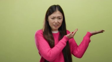 Pembe kazaklı kadın parlak yeşil arka planda el hareketleriyle kafa karışıklığını ifade ediyor.