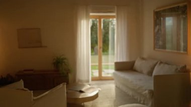 Akdeniz lüks oturma odası bej dekorlu, güneş ışığı katıksız perdelerin arasından modern mobilyalara ve yumuşak bir halıya vuruyor, davetkar bir sükunet ortamı yaratıyor..