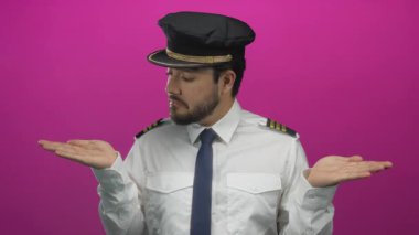 Üniformalı genç İspanyol pilot, parlak pembe arka plana el uzatarak havacılık bağlamında seçim ve karar veriyor..
