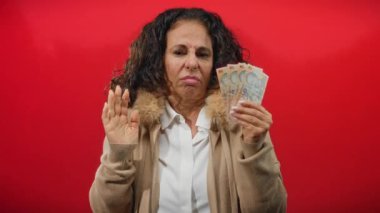 Kadın, Romanya 'nın parasını elinde tutan kırmızı bir zemine karşı belirsiz bir ifadeyle, finans ve duygu temalarını yakalıyor.