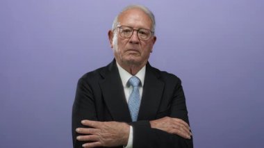 Gözlüklü kıdemli bir adam mor bir geçmişe, kollarını kavuşturup otorite ve profesyonelliğe karşı güvenle ayakta duruyor..