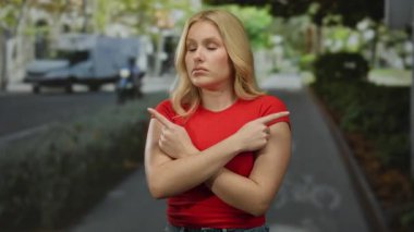 Şehir caddesinde kırmızı tişörtlü, sarı saçlı bir kadın farklı yönleri işaret ederek şehir ortamında kafa karışıklığı ve karar verme mekanizmasını taşır..