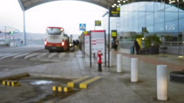 Bulanık görüntü, dışarıda park etmiş bir otobüsle bir havaalanı terminalinin odaklanmış görüntüsünü gösteriyor. Binen insanları, büyük cam bir yapının altında dinamik bir seyahat sahnesi yaratırken yakalıyor..