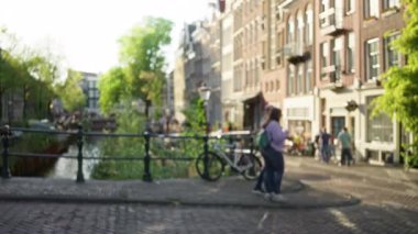 Amsterdam 'da şehir manzarası bulanık. Yürüyen insanlar, bisikletler ve tarihi mimari. Kanal caddelerini açık bir öğleden sonra gökyüzünün altında kaplıyorlar..