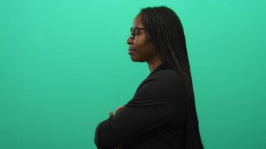 Örgülü ve gözlüklü kendine güvenen bir kadın yeşil arka plana gülümsüyor, zarafet ve profesyonellik sergiliyor.