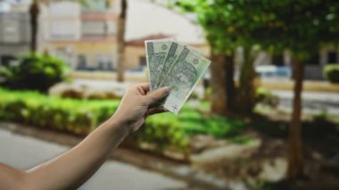 Şehir dışındaki bir sokak ortamında elinde Polonya zloti banknotları tutan bir adam. Arka planda gün ışığı altında kentsel yeşillik var..